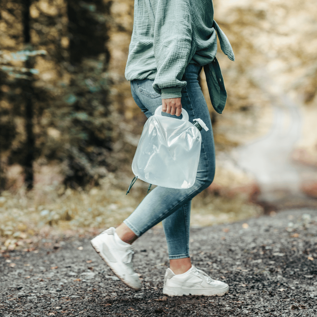 Eine Person mit Jeans und Sneakers trägt einen vollen Wasserkanister. 